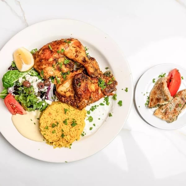 A plate of roasted chicken, yellow rice, Greek salad, and a side of spinach pie.