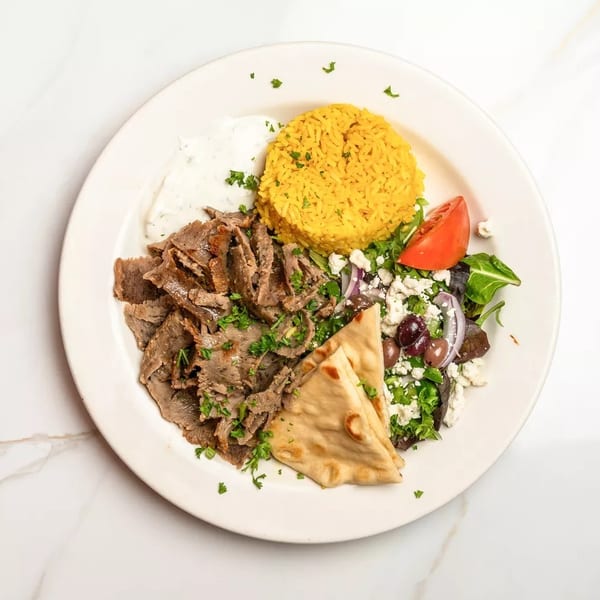 A gyro platter with sliced meat, yellow rice, Greek salad, pita bread, and tzatziki sauce.