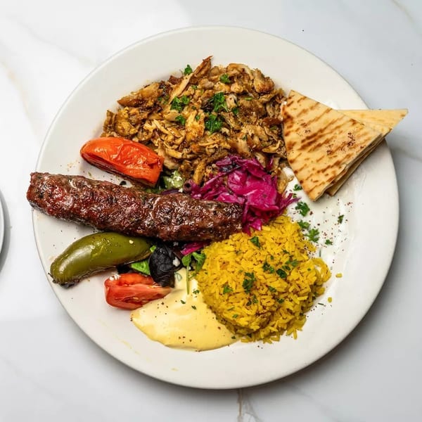 A white plate with chicken shawarma, kebab, yellow rice, grilled vegetables, and pita bread.